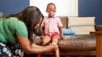 boy with scraped knee on couch and woman tending to wound